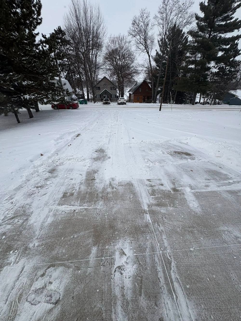 Snow-covered driveway leading to houses among winter trees. Clear signs of recent snow removal.