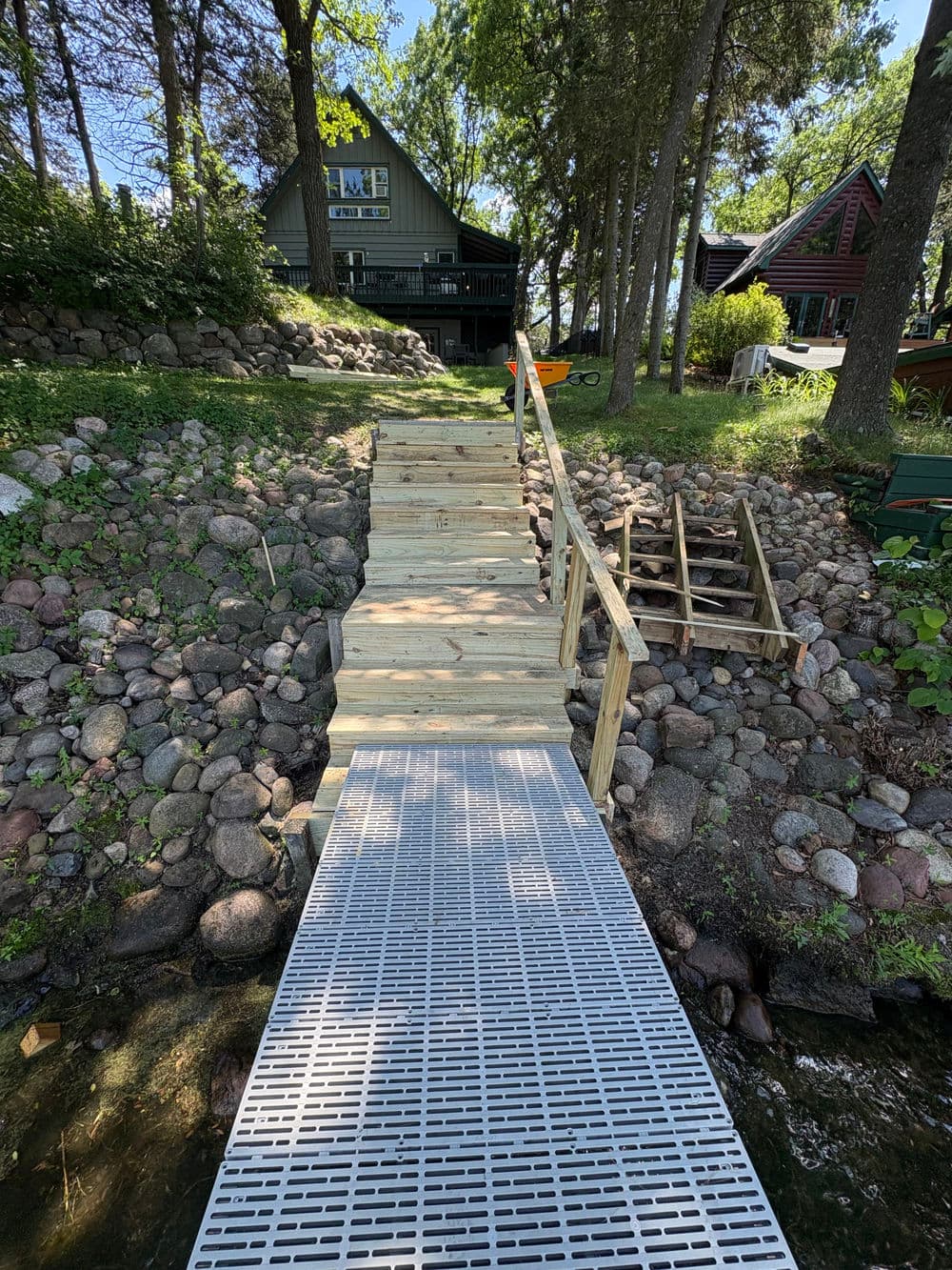 Wooden stairs leading to a lakefront cabin with a dock and rocky shoreline.