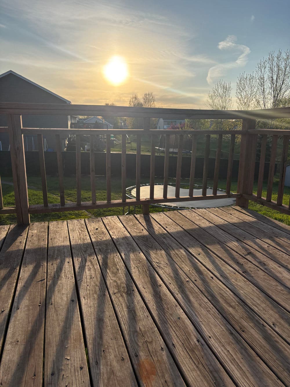 Sunset view from a wooden deck, highlighting shadows on the floor and a lawn in the background.