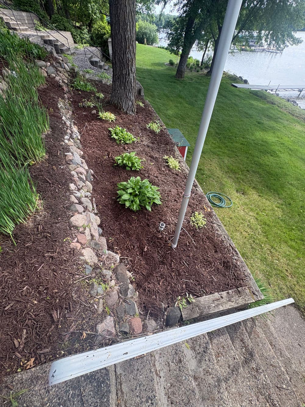 Landscaped garden with mulch, flowers, and a view of the lake on a sunny day.