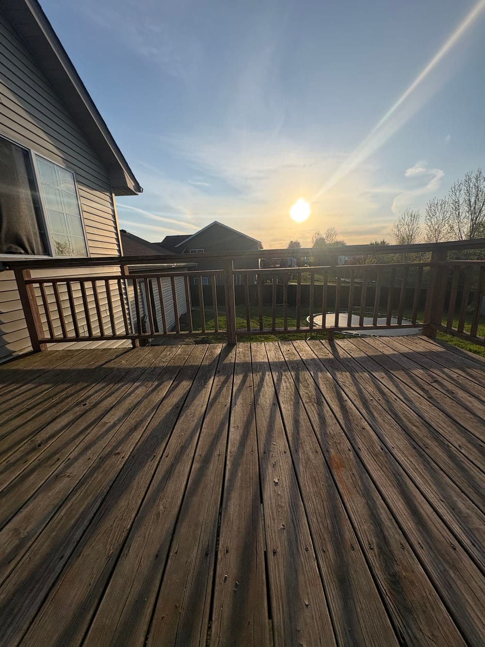 Sunset view from a wooden deck, showcasing a tranquil backyard landscape and clear skies.