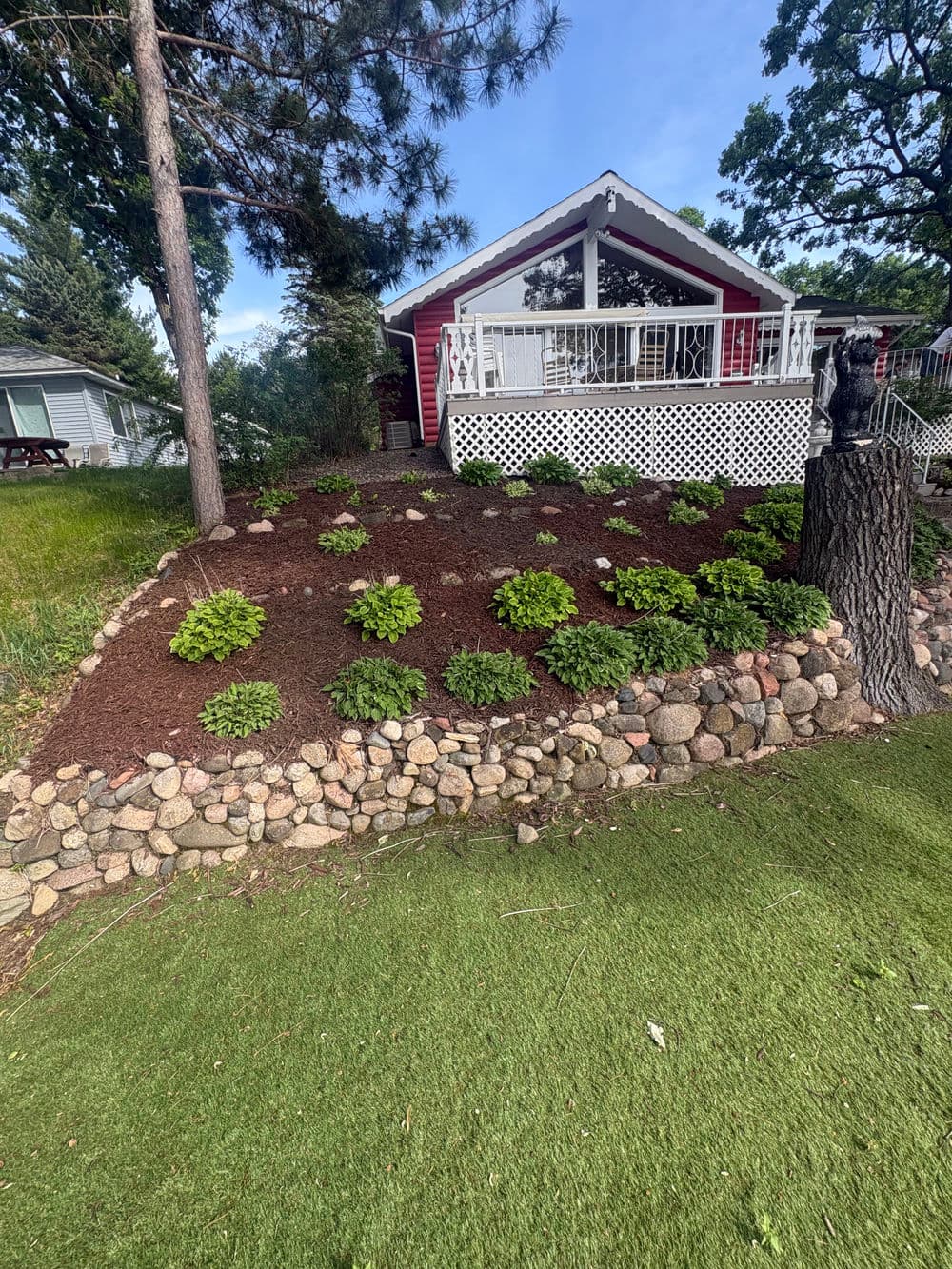Decorative garden with mulched flower bed and stone border in front of a red house.