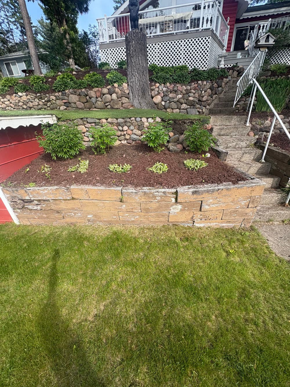 Landscaped garden with stone retaining wall, green plants, and well-maintained lawn.