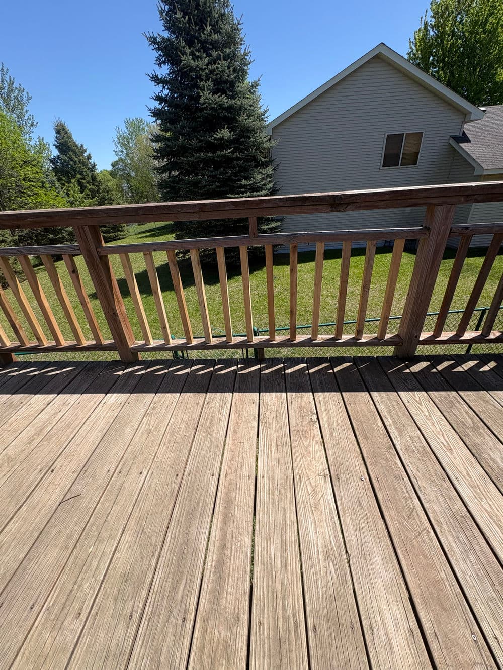 Wooden deck overlooking a green lawn and trees under a clear blue sky.