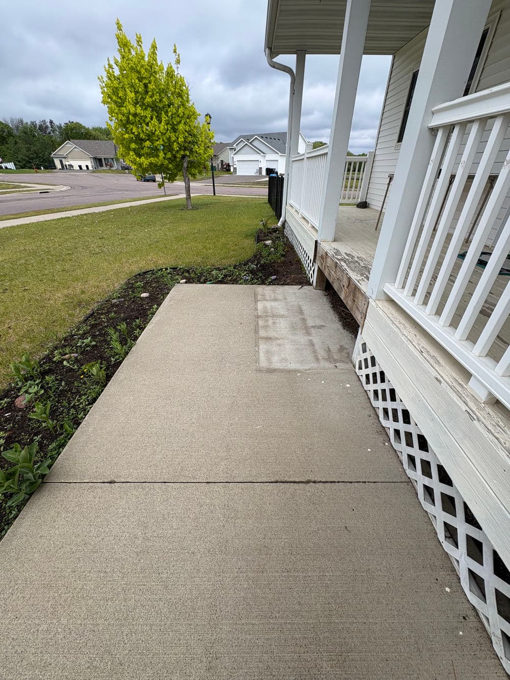 Concrete sidewalk and porch with landscaping and a yellow tree beside a suburban home.
